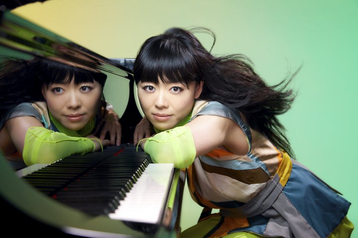 hiromi draped across her piano, her face reflected above the keys